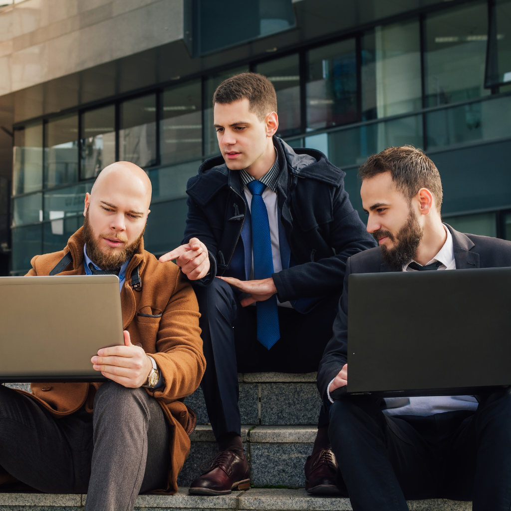 three men looking at a laptop sitting on stairs