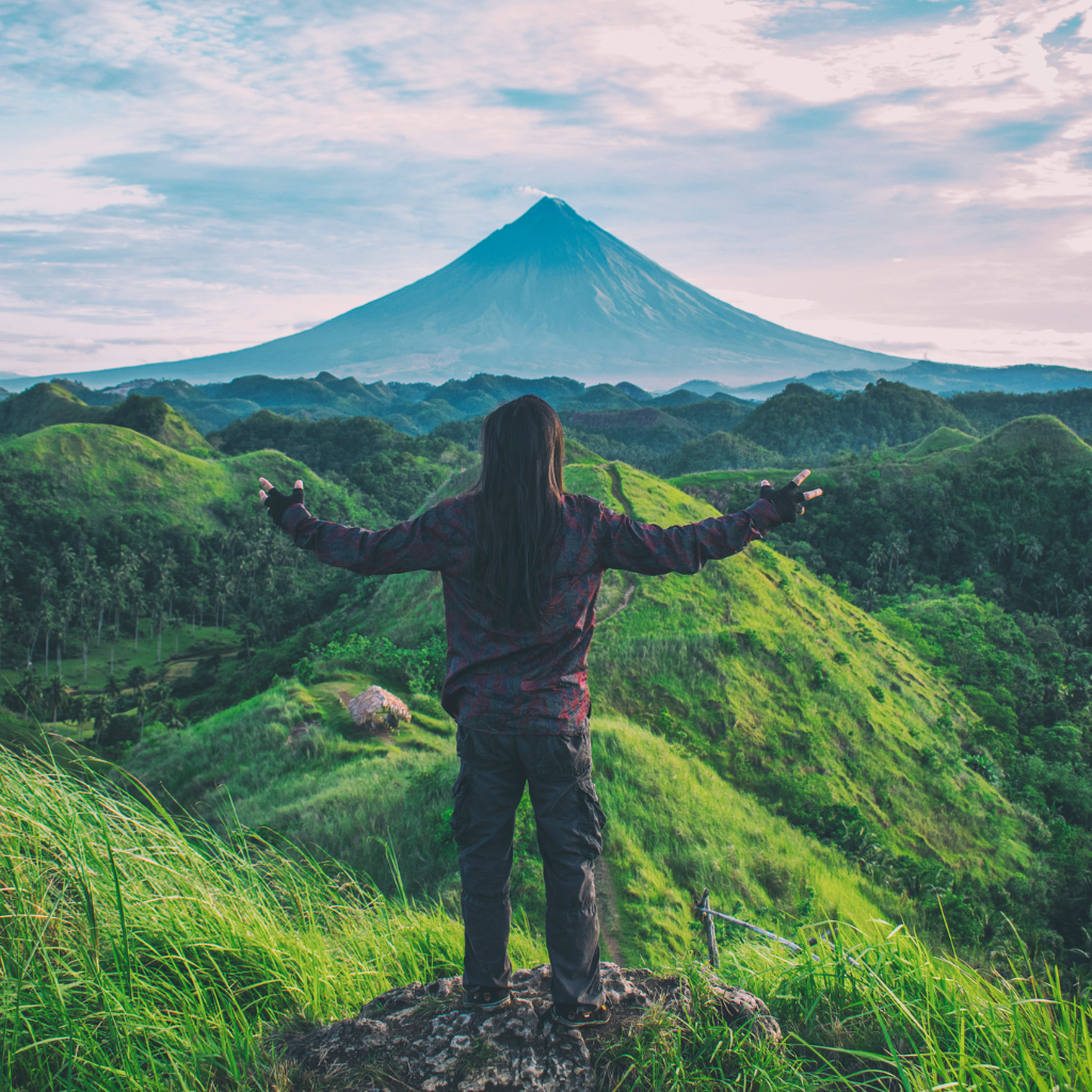 a man with is back to the camera exclaiming over the view of a volcano in the distance