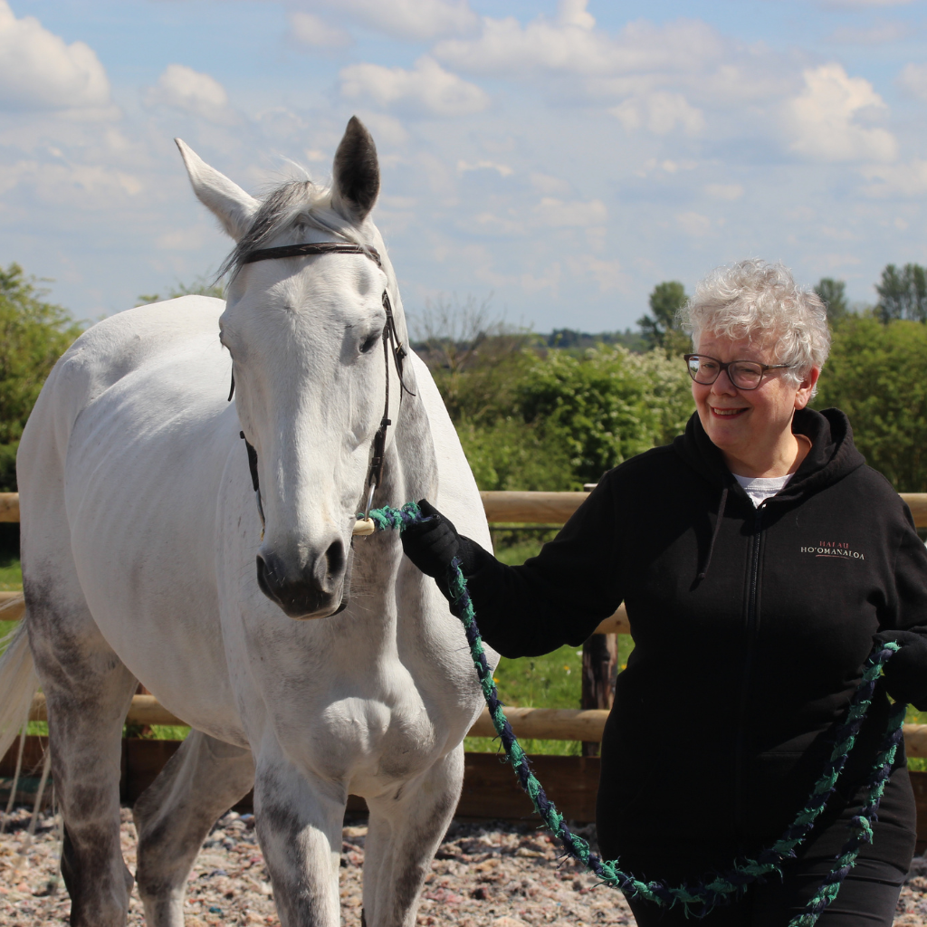 a woman in a black fleece leading a white horse