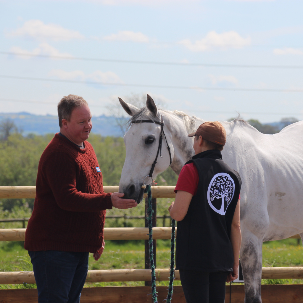 a man touching a horses nuzzle whilst talking to someone