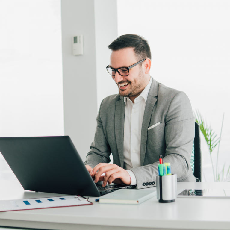 a man typing on a laptop and smiling whilst taking a. virtual meeting