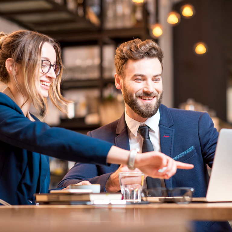 a man and woman in blazers pointing at a laptop and smiling