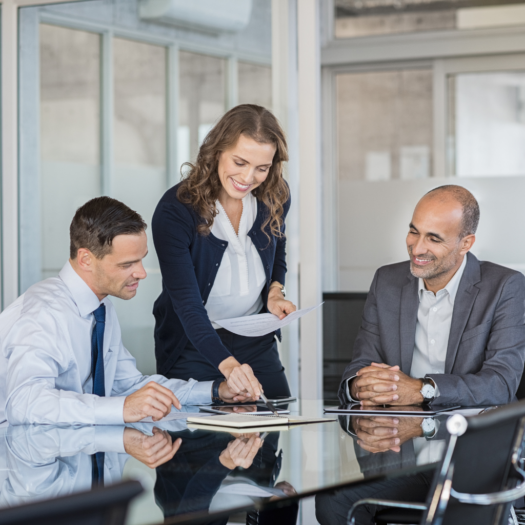 a woman leaning over a meeting table with two men sitting at the table